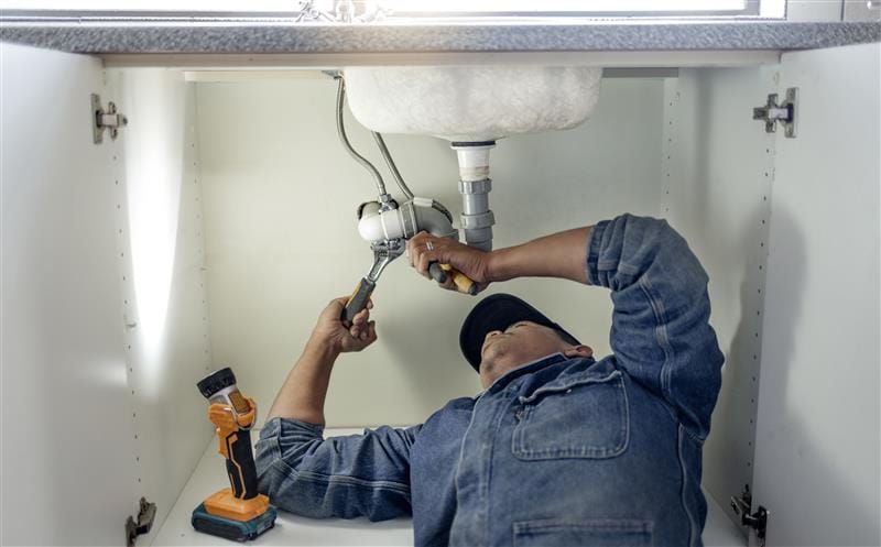 Plumber repairing pipes beneath a bathroom sink in Morgan Hill