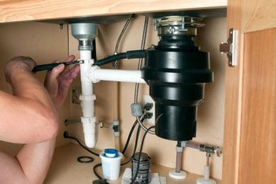 Plumber repairing a garbage disposal beneath a kitchen sink in Morgan Hill