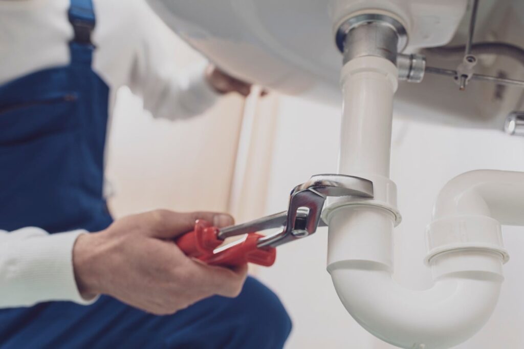 Plumber repairing a white drain pipe beneath a sink in Morgan Hill